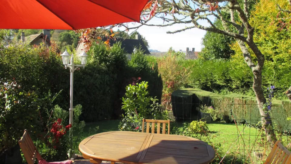 Table and chairs under a red parasol in a sunny garden.