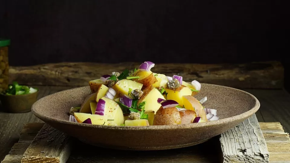 A bowl of roasted potato and onion salad placed on a wooden block.