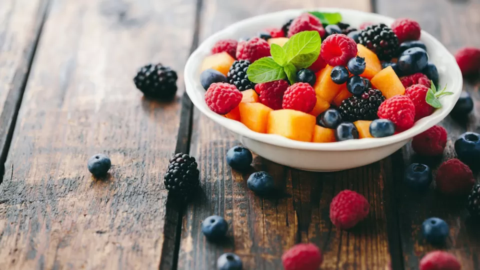 A bowl of fresh fruit salad garnished and placed on a wooden table.